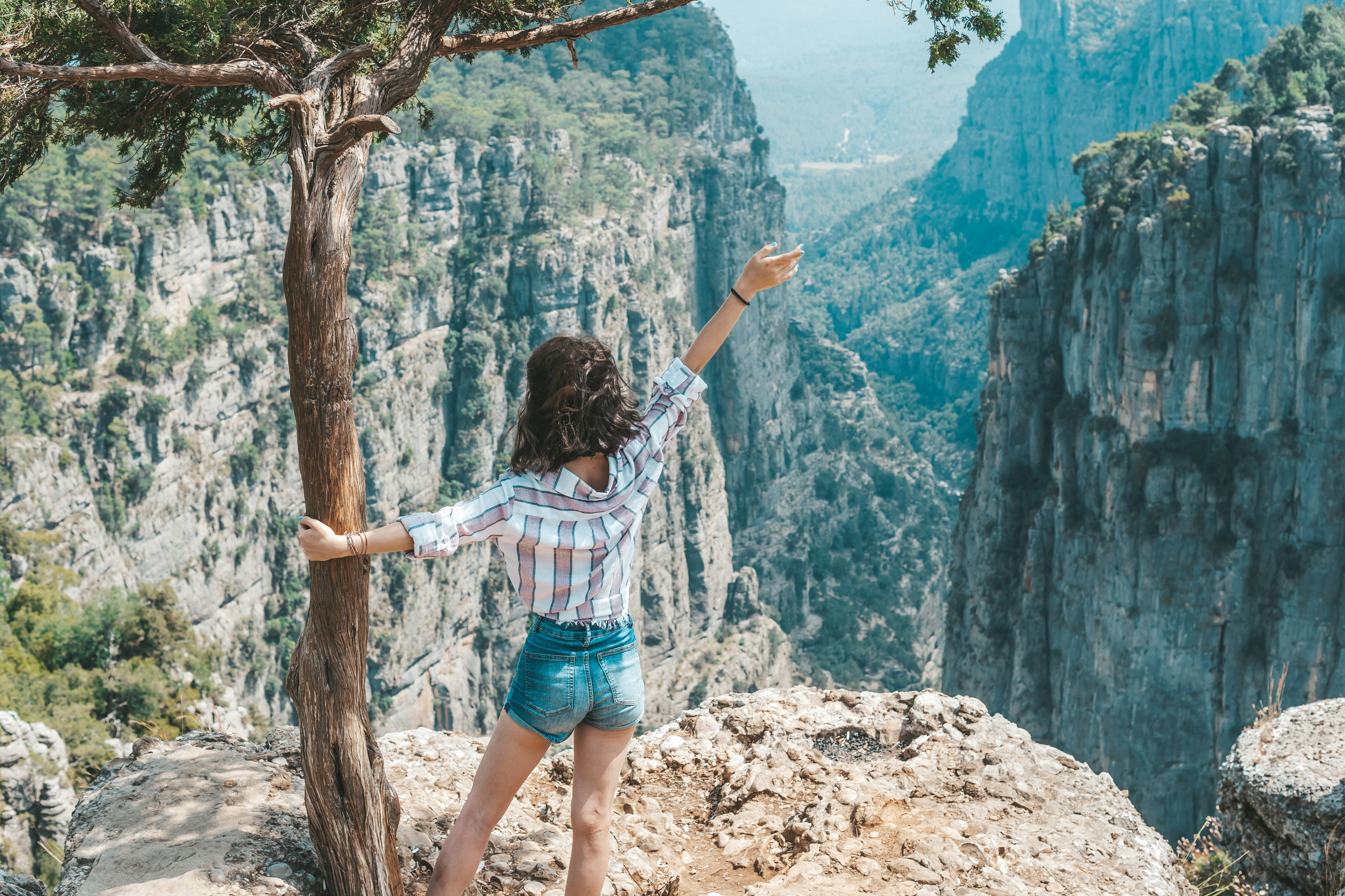 woman in white shirt and blue denim shorts standing on brown tree branch during daytime